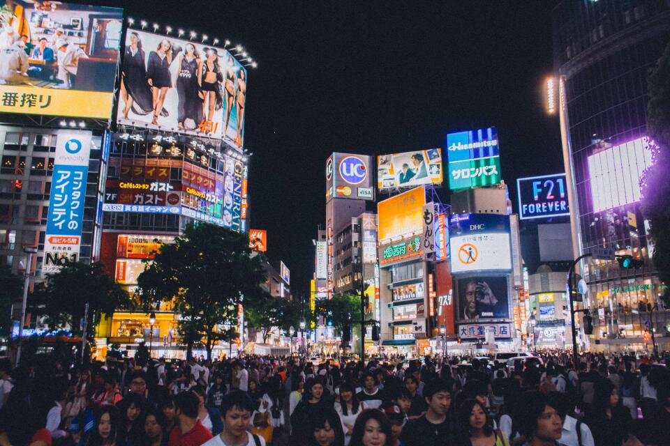 밤 도심 교차로 건물마다 광고판이 빼곡히 붙어 있고 아래로 인파가 지나가는 모습