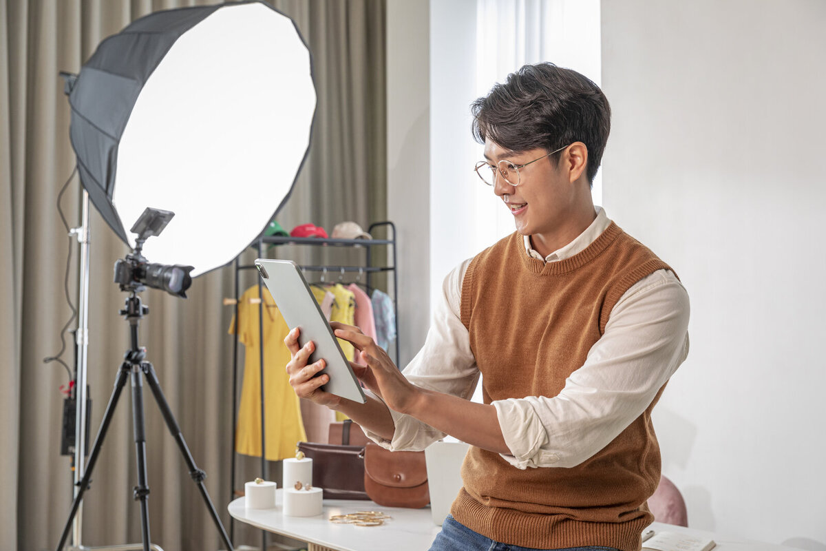 옷걸이와 조명 앞에서 태블릿으로 상품 사진을 확인하는 남성 판매자